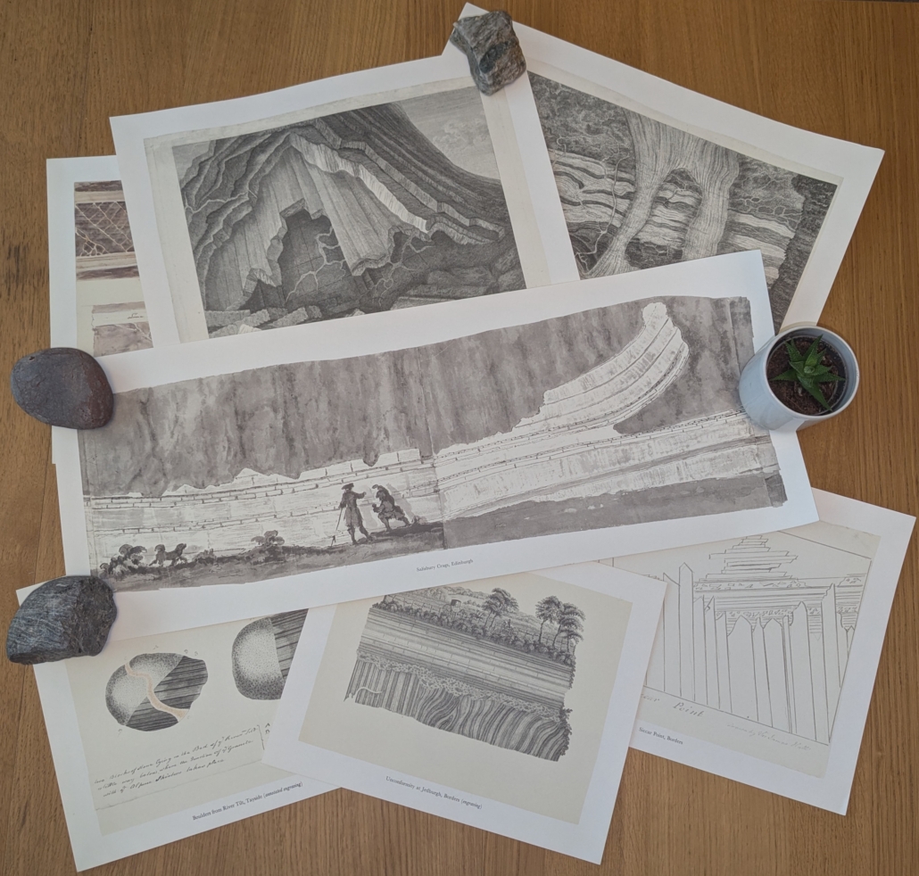 Lost-Drawings-1 Photograph of a selection of seven prints of the lost drawings. There are lots of different sizes and aspect ratios of the drawings. Some of them are quite wide and are held down with rocks. Most prints are in greyscale and are of pencil or ink sketches or engravings, but some have some light watercolour. The sketches are of a range of geological features, including folded rocks, veining, geological maps, and unconformities.